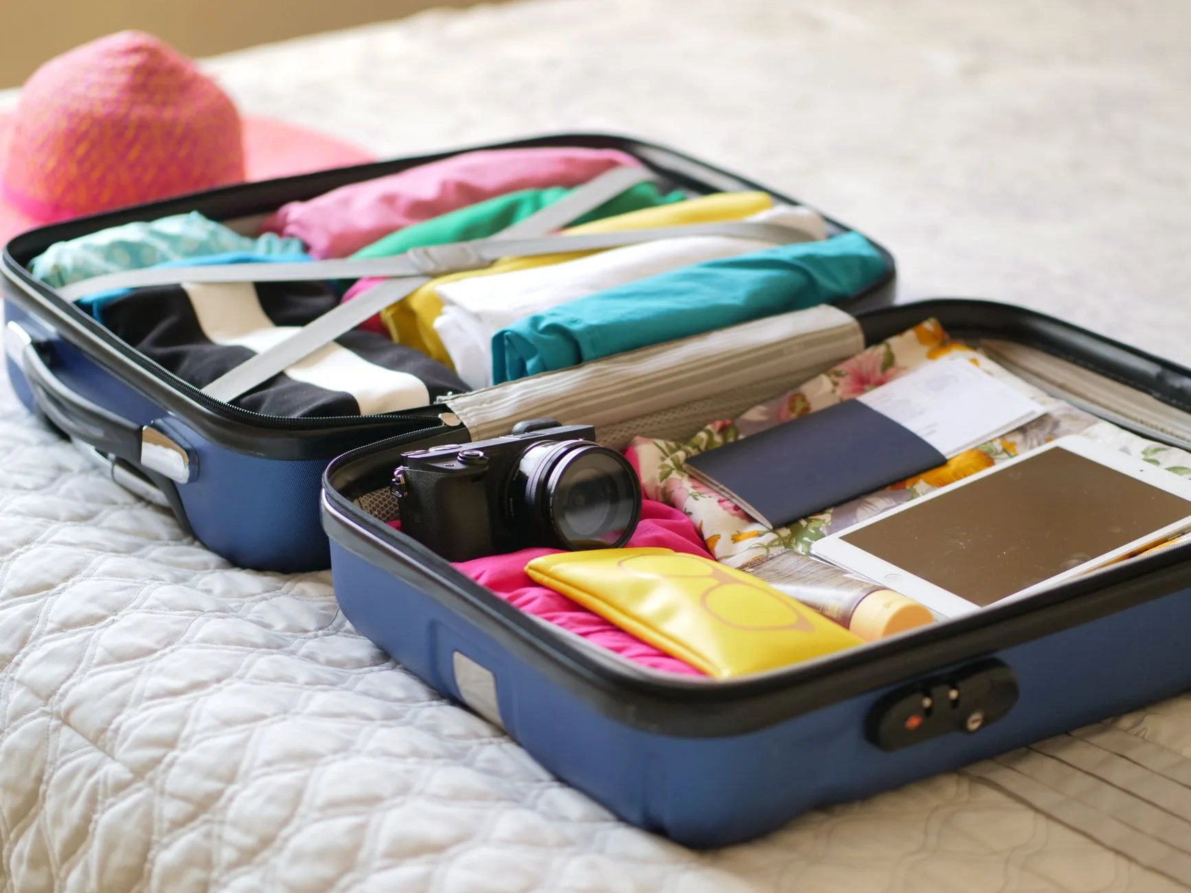 Valise ouverte sur un lit avec passeport, appareil photo, tablette et vêtements pliés